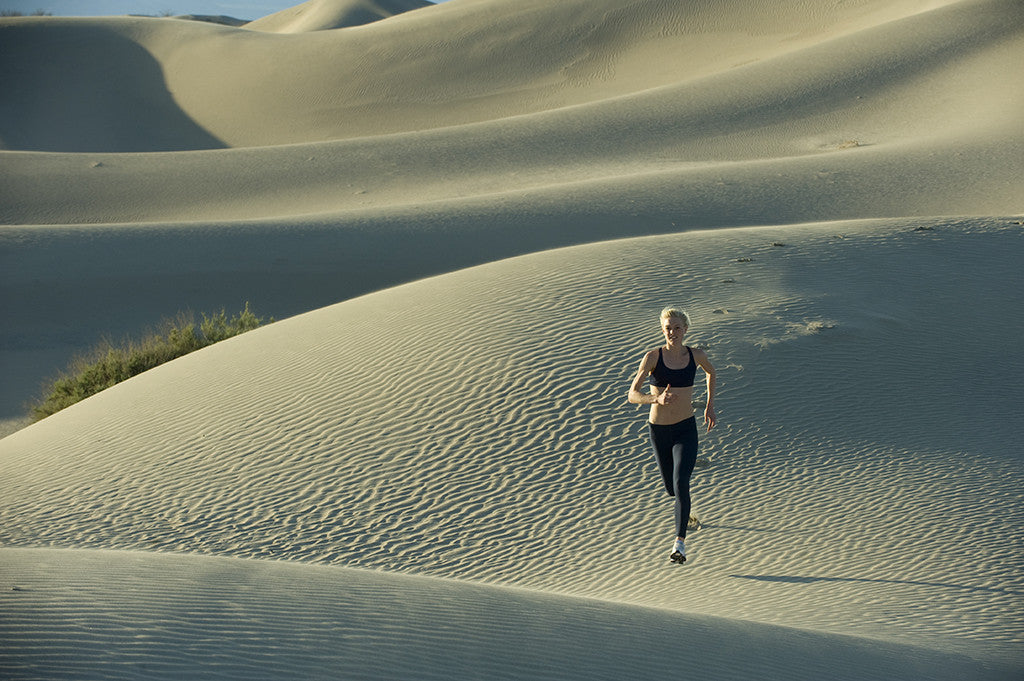 Female runner running across dunes in the desert