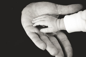 A black and white photos of a child's hand placed in an adults hand.