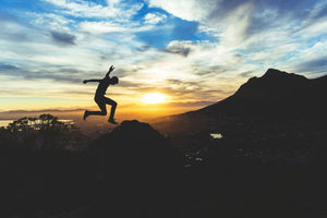 Man jumping in the mountains with the sun setting in the distance