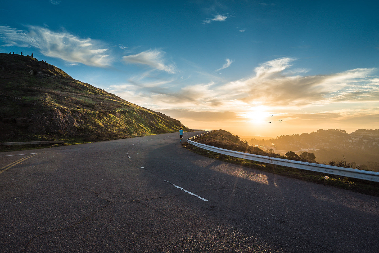 Male runner running along a mountain road as the sunrises